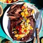 A plated Grilled Asian Flank Steak that has been sliced and topped with Pineapple Salsa in the sunlight.