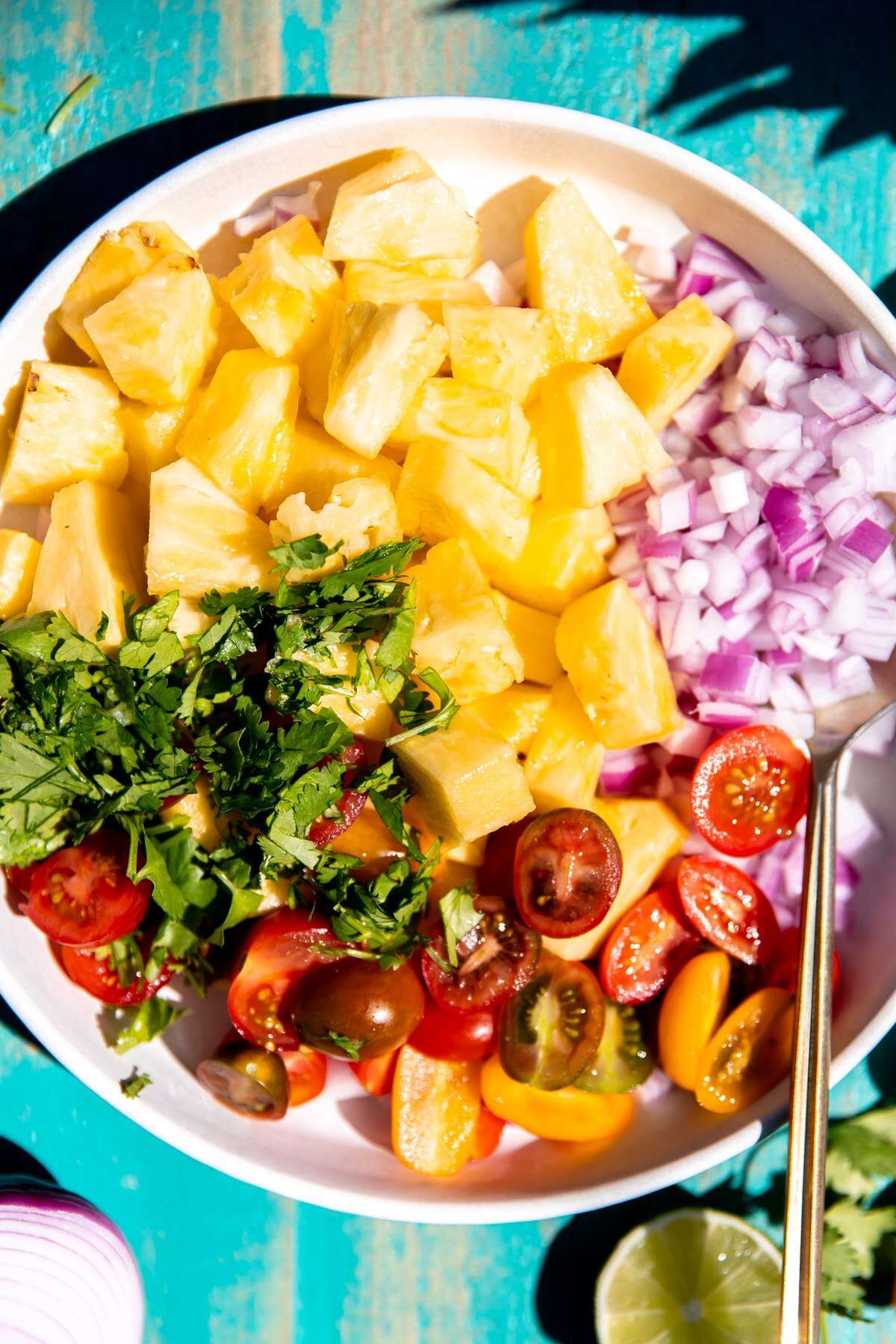 A bowl of pineapple salsa with all of the ingredients in separate piles waiting to be mixed together. 