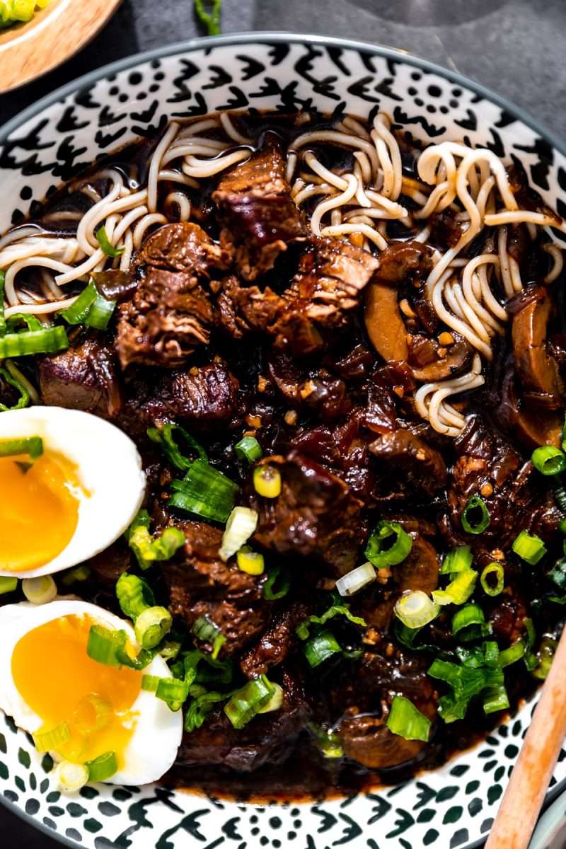 A close-up photo of beer braised beef ramen topped with soft boiled eggs and diced green onion.