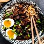 Beer braised beef ramen in a bowl topped with soft boiled eggs and diced green onion.
