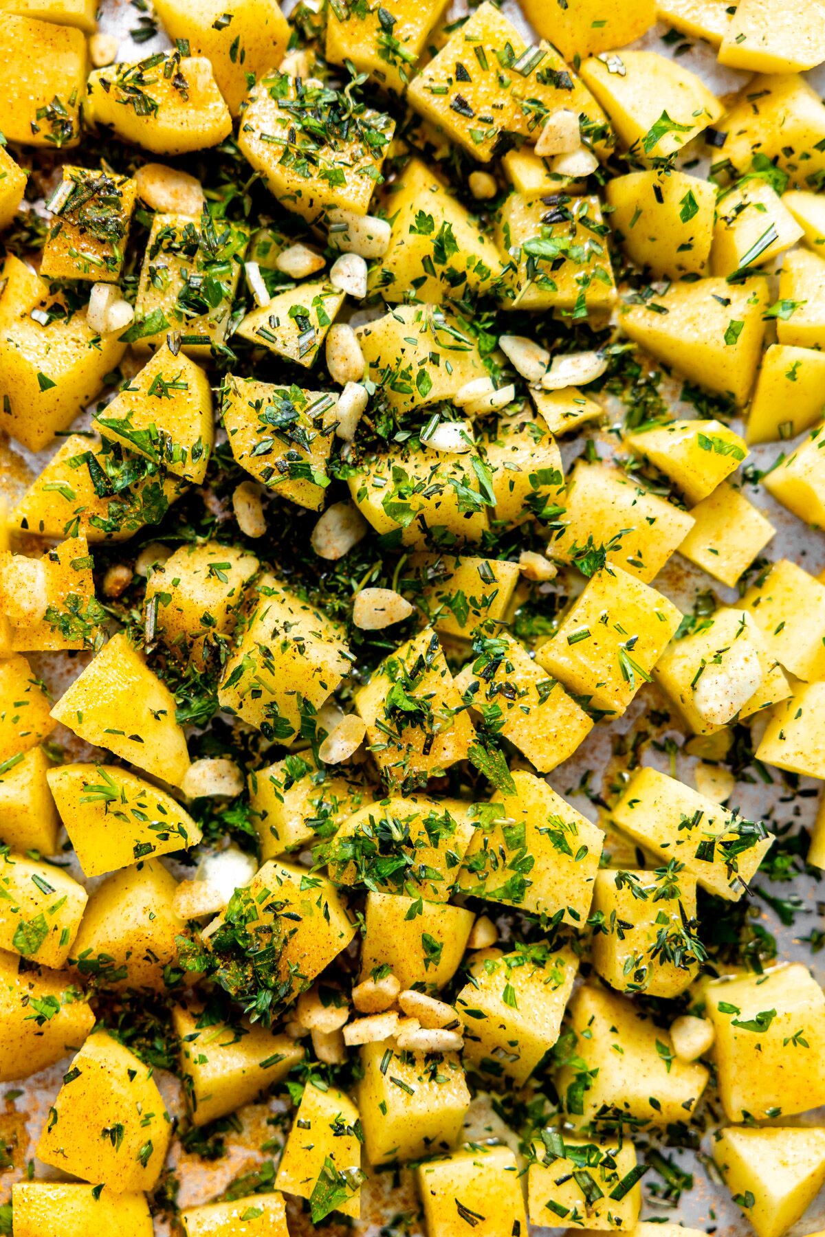 Cut potatoes on a sheet pan with garlic and herbs ready for the oven. 