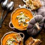Roasted Butternut Squash Soup served in festive bowls topped with goat cheese crumbles and pumpkin seeds.
