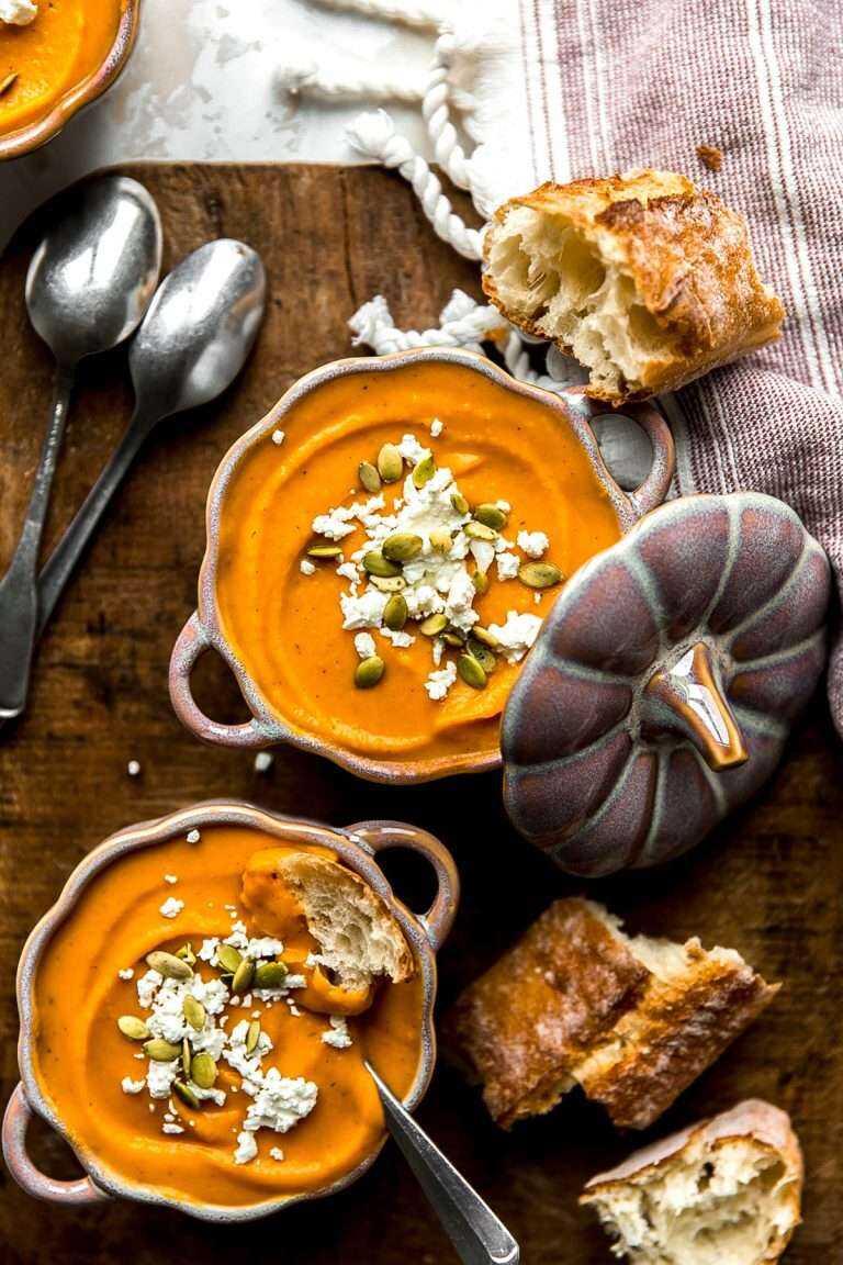 Roasted Butternut Squash Soup served in festive bowls topped with goat cheese crumbles and pumpkin seeds.