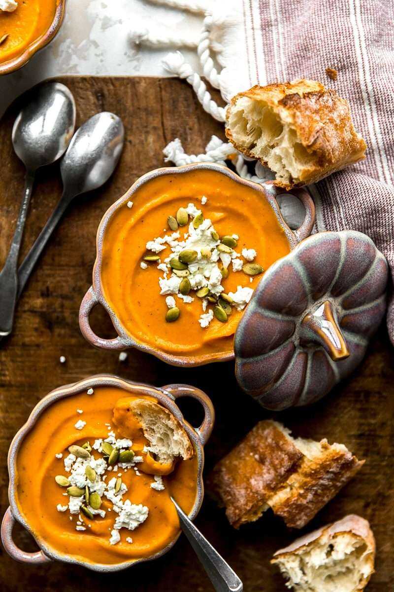 Roasted Butternut Squash Soup served in festive bowls topped with goat cheese crumbles and pumpkin seeds.