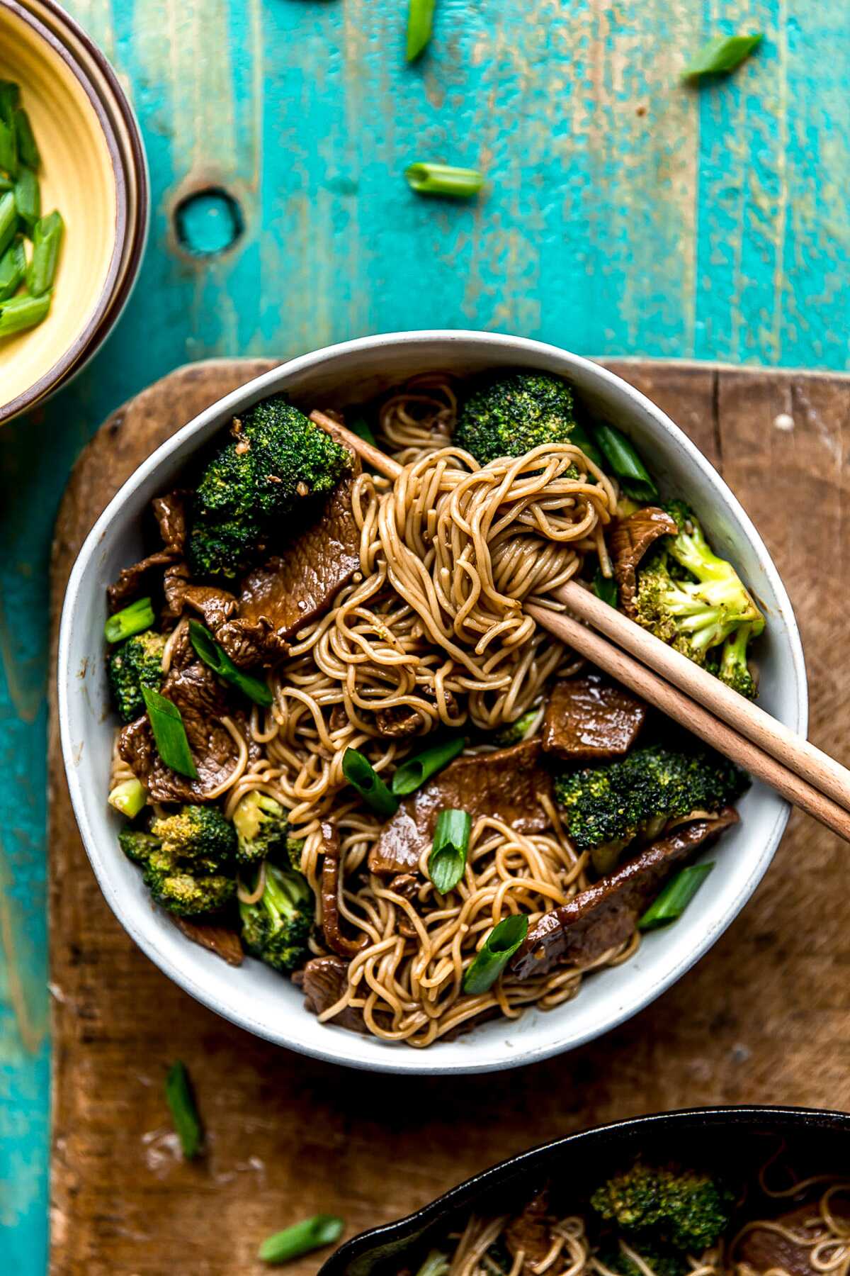 Chopsticks digging into a bowl of teriyaki beef and broccoli noodles.