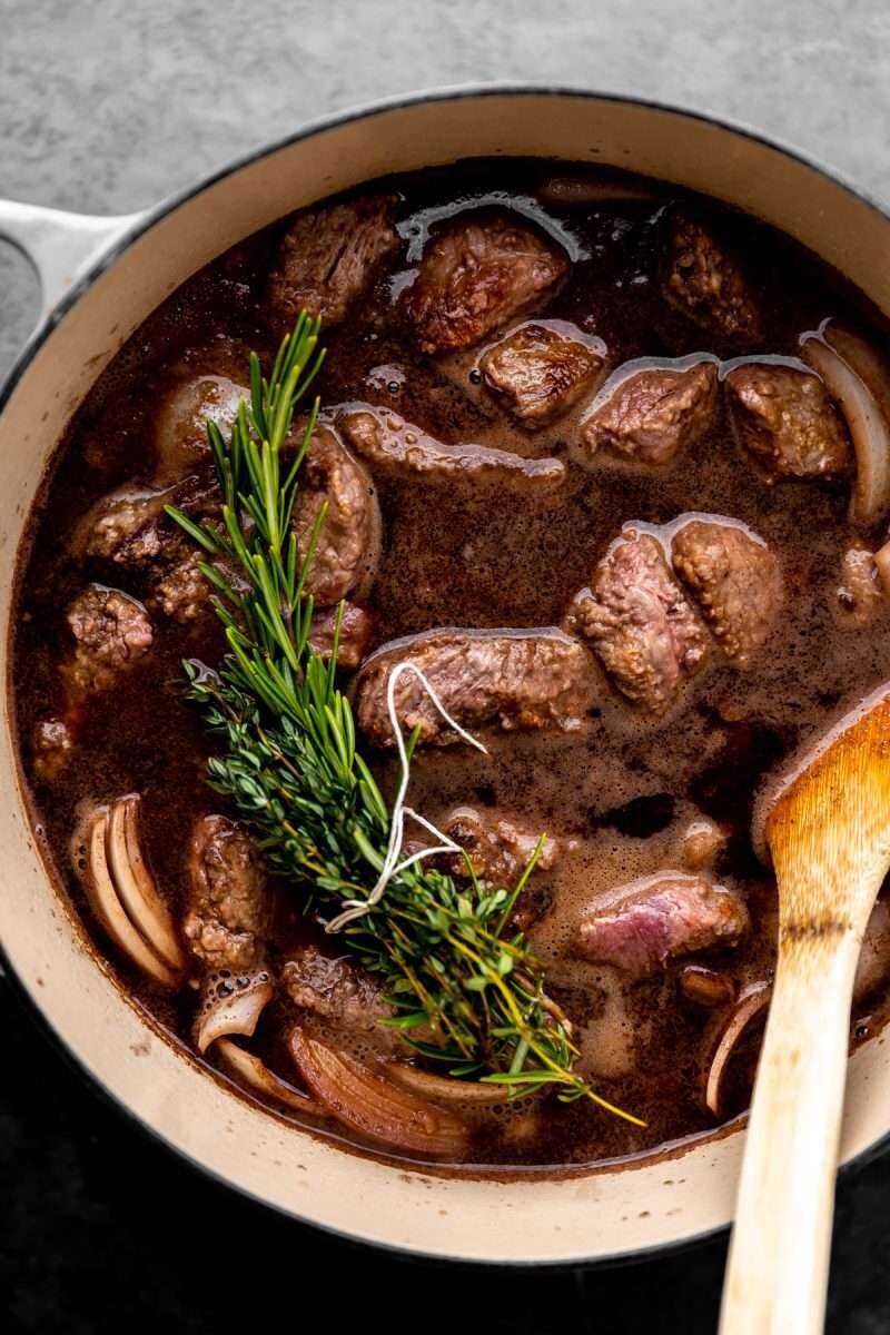 Seared beef tips in a Dutch oven with red wine and herbs.