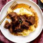Red Wine Braised Beef Tips on a bed of mashed potatoes on a white plate.