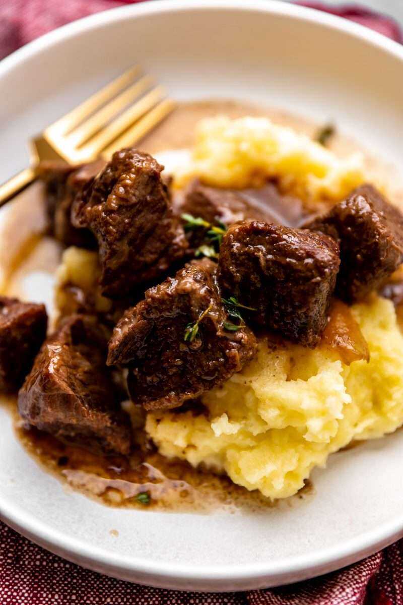A close-up photo of red wine braised beef tips on mashed potatoes.