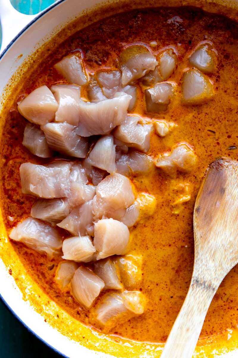 The chicken being added to the coconut curry sauce.