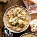 A bowl of Chicken and Dumplings Soup with spoons and baguettes around.