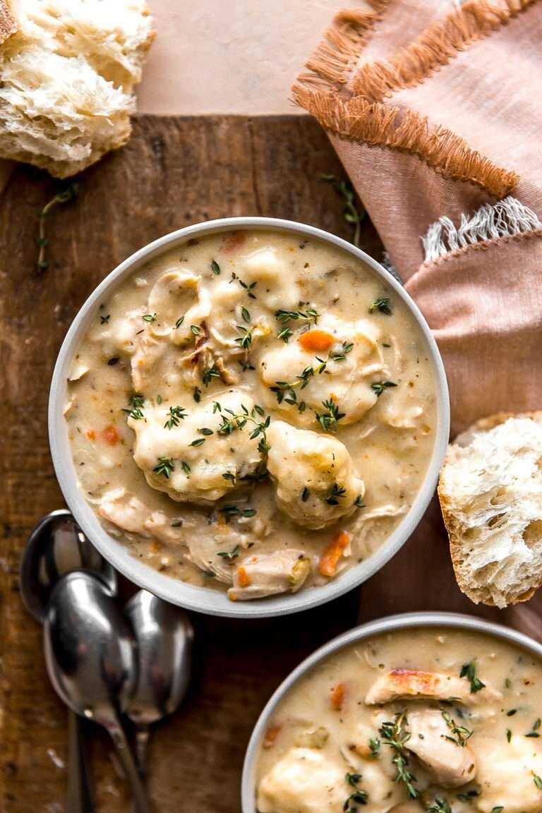 A bowl of Chicken and Dumplings Soup with spoons and baguettes around.