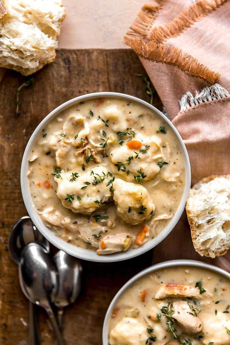 A bowl of Chicken and Dumplings Soup with spoons and baguettes around.