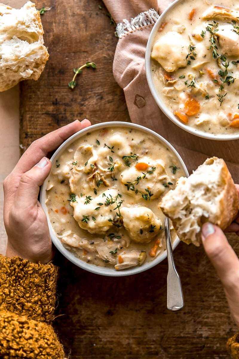 Hands holding onto a bowl of soup and dunking a piece of baguette into the bowl.