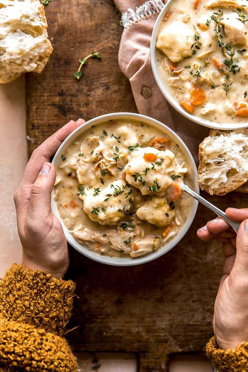 Hands holding onto a bowl of Chicken and Dumplings Soup with a spoonful coming out of the bowl.
