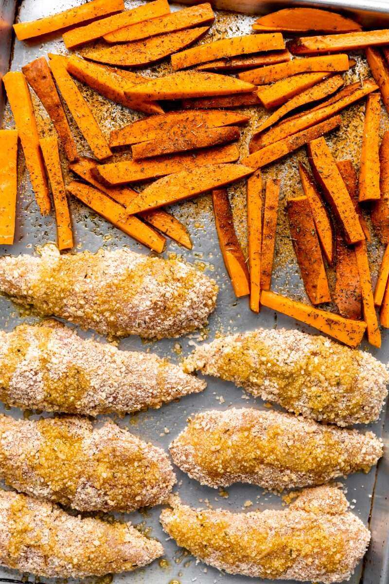 Sweet potato fries and breaded chicken fingers on a sheet pan prior to baking. 