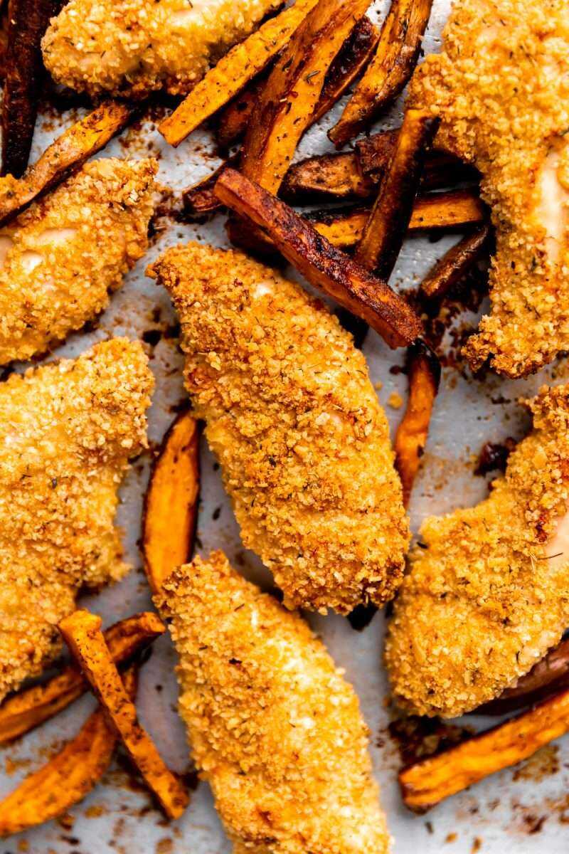 Crispy parmesan chicken fingers on a sheet pan with sweet potato fries