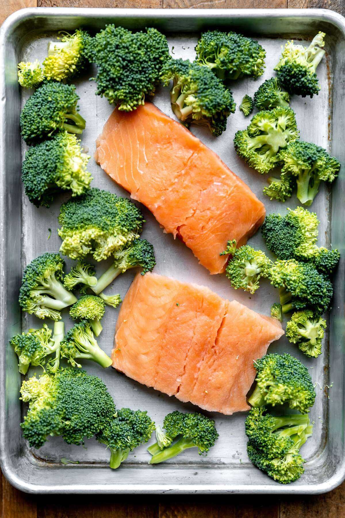 Raw salmon filets and broccoli on a sheet pan.