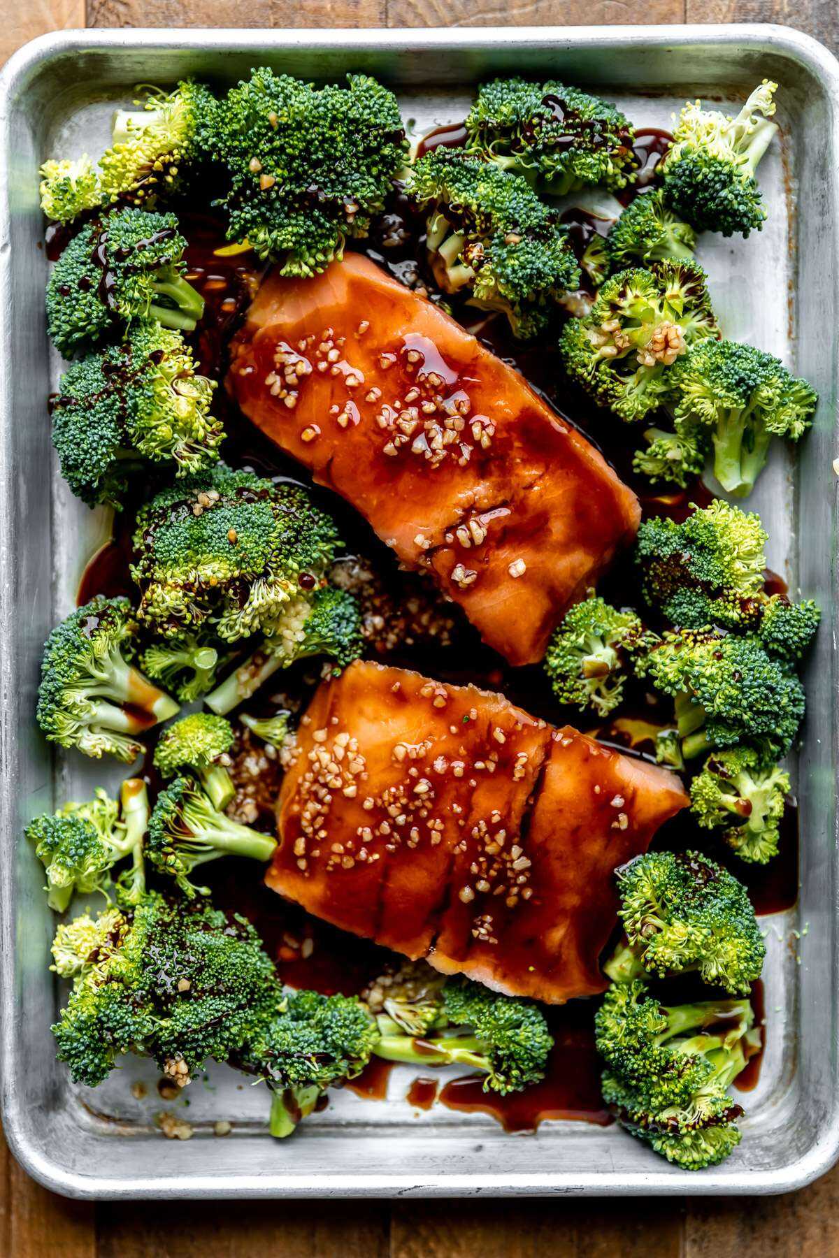 Raw salmon and broccoli on a sheet pan with the teriyaki sauce poured over top.