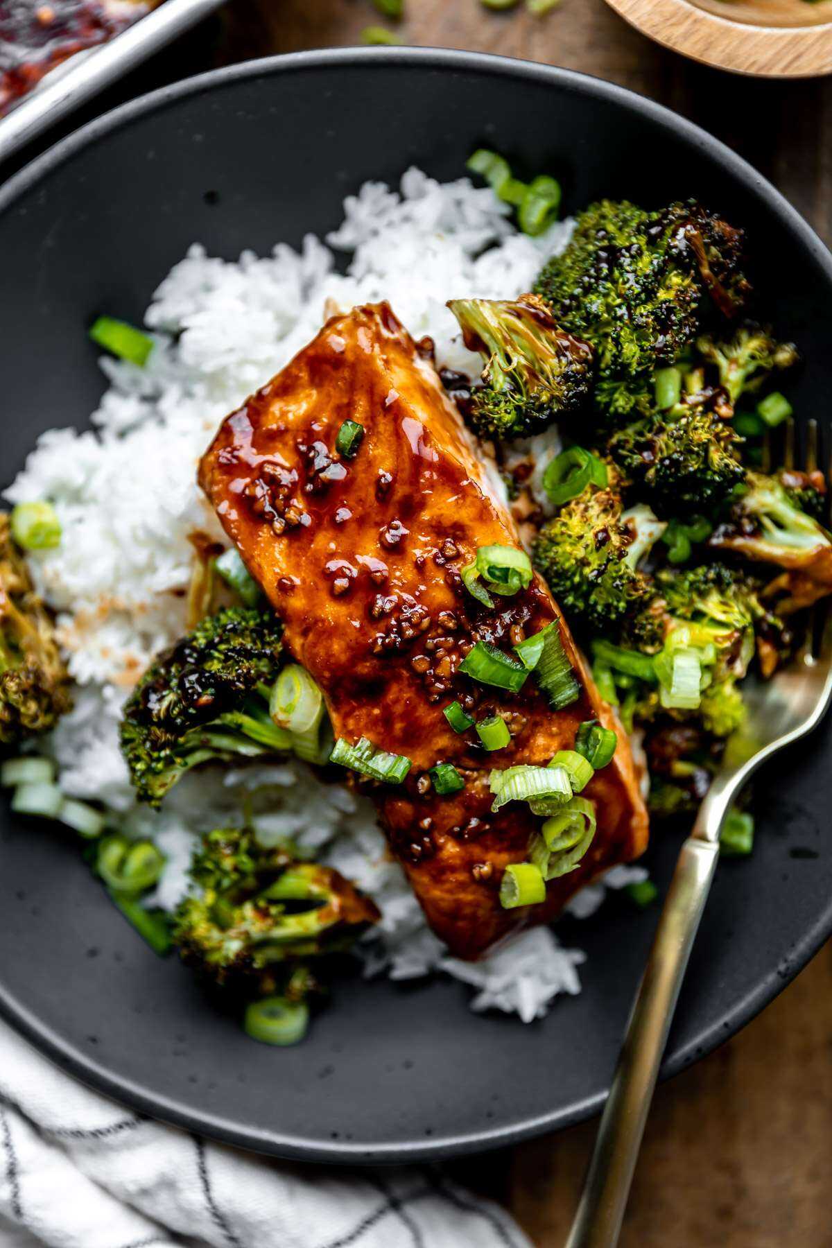 A close-up photo of a roasted salmon filet and broccoli over white rice.