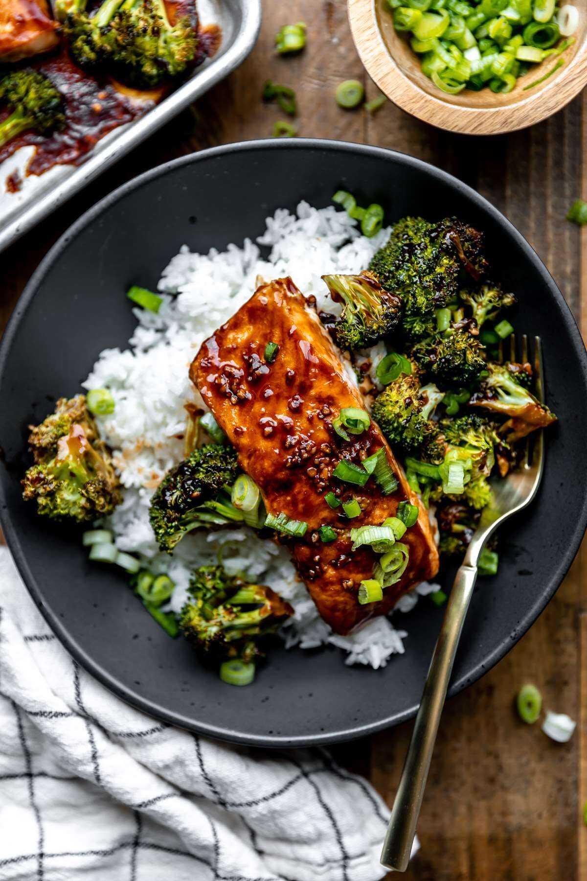 Plated Sheet pan teriyaki salmon & broccoli over white rice in a black bowl. 