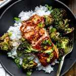 Sheet pan teriyaki salmon & broccoli plated on top of a bed of white rice in a black bowl with the salmon flaked apart.