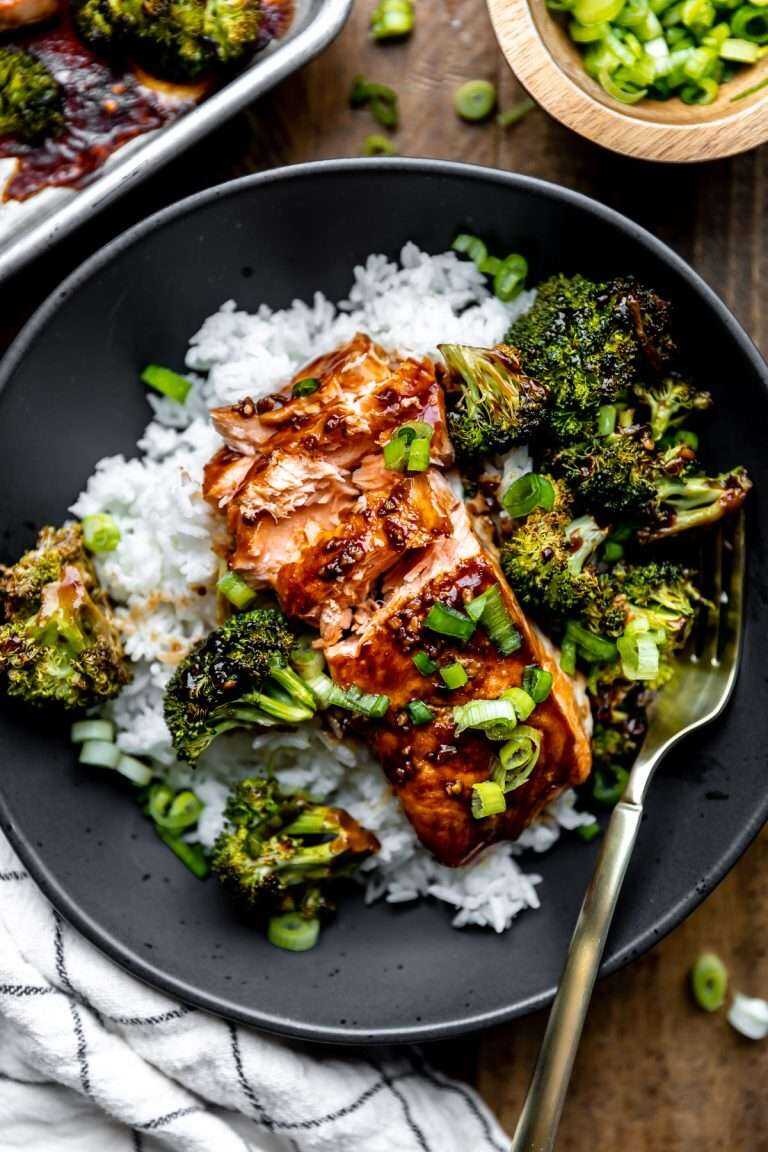 Sheet pan teriyaki salmon & broccoli plated on top of a bed of white rice in a black bowl with the salmon flaked apart.