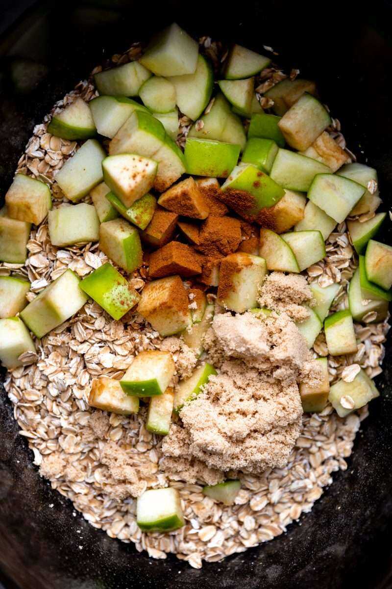 an overhead phot of old fashion oats, sliced granny smith apples and cinnamon in a crockpt. 