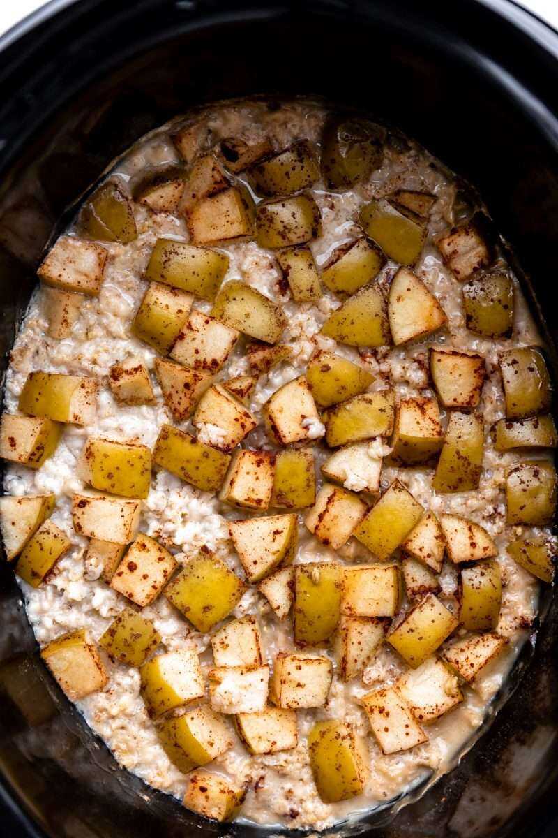 an overhead photo of oats, granny smith apples, cinnamon, and milk cooking in a crockpot.