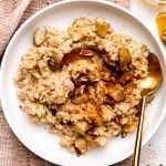 Overhead photo of oatmeal in a white bowl topped with apples and cinnamon with a gold spoon laying in oatmeal.