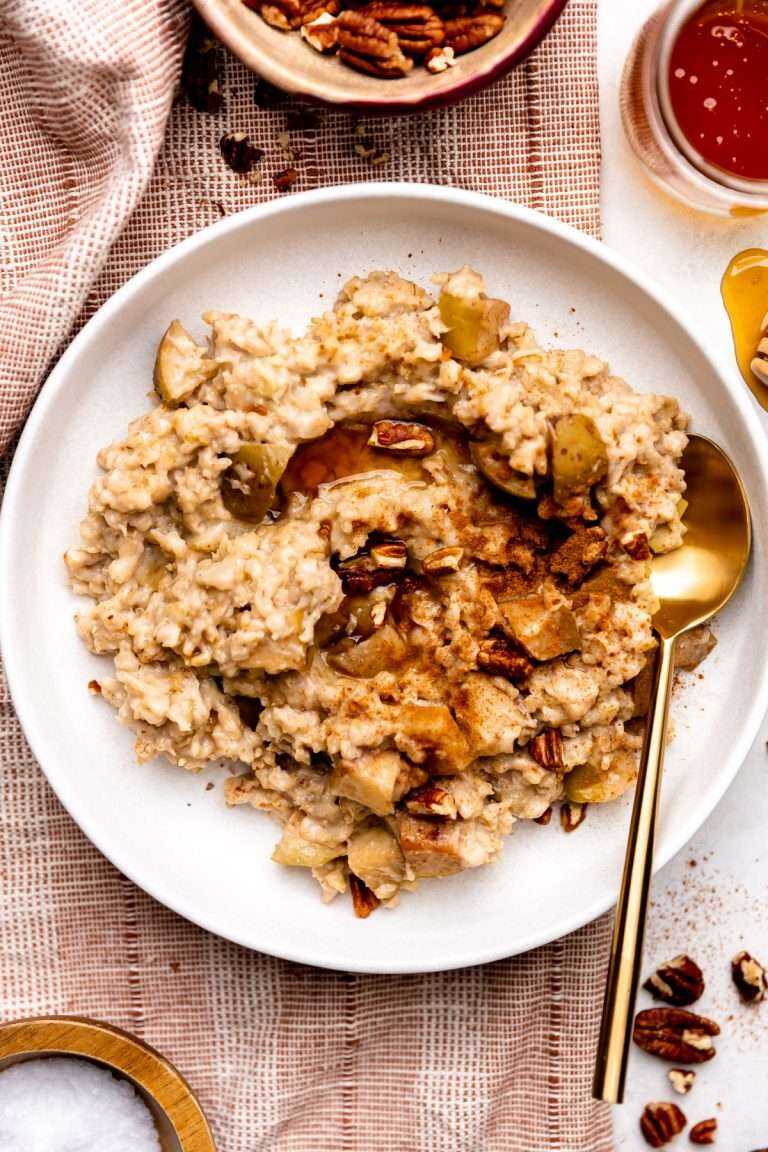 Overhead photo of oatmeal in a white bowl topped with apples and cinnamon with a gold spoon laying in oatmeal.