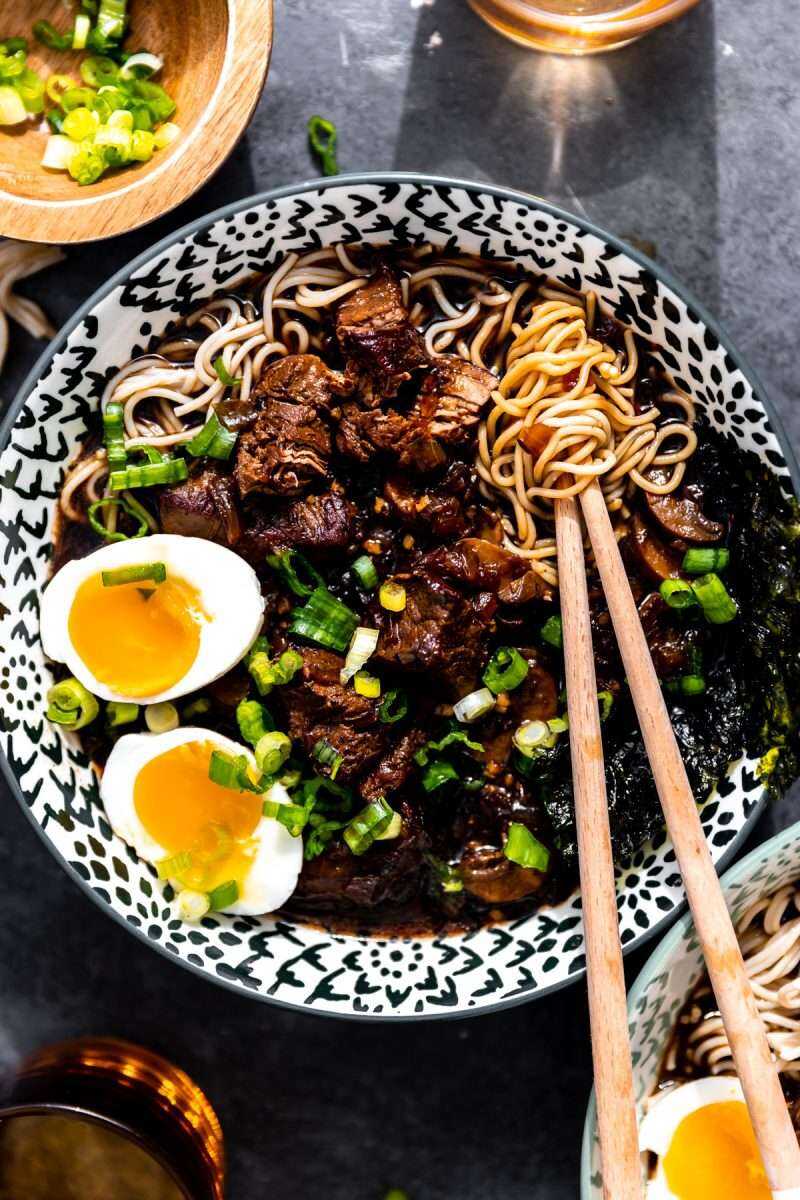 Beer braised beef ramen in a bowl topped with soft boiled eggs and diced green onion.