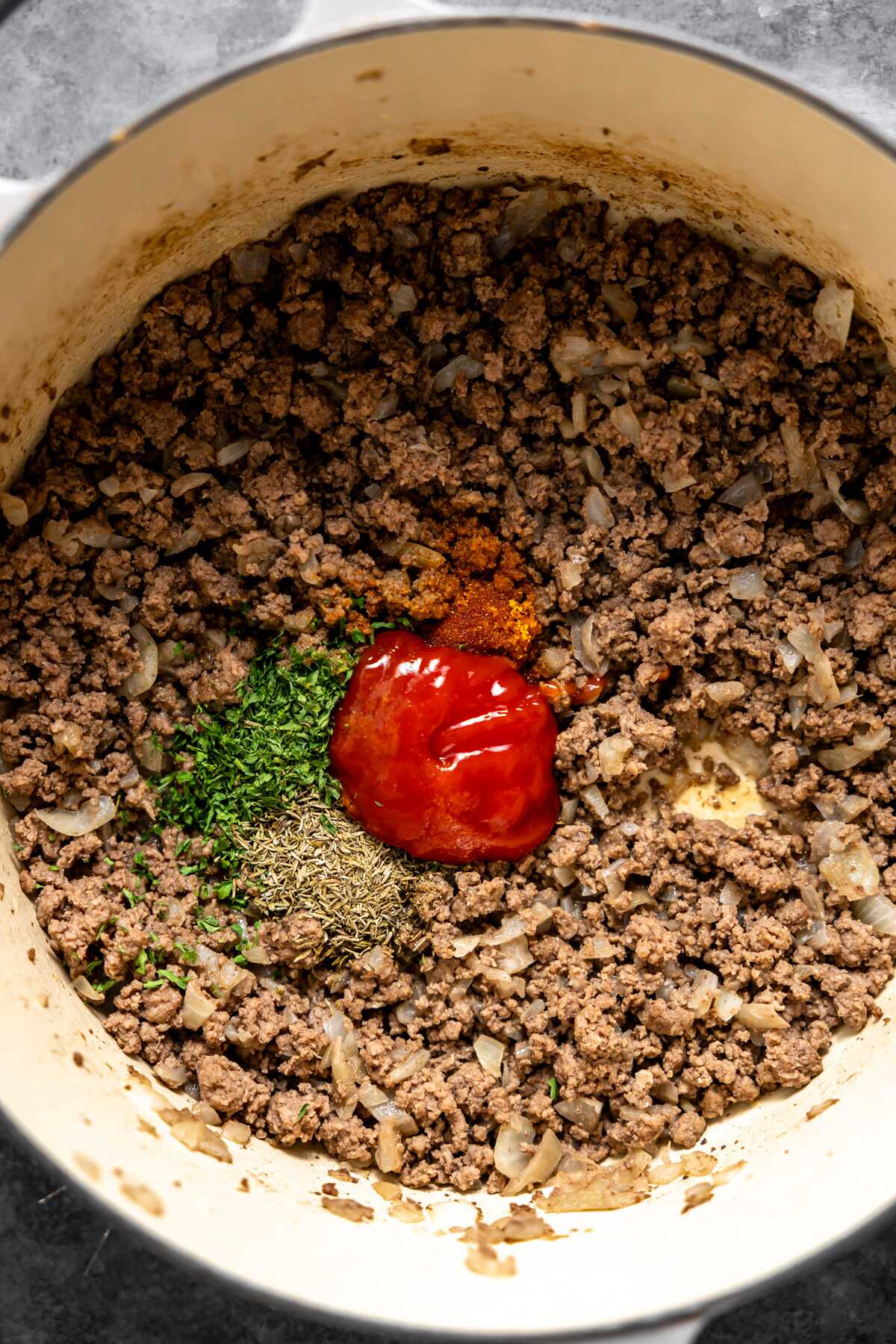 Browned ground beef in a stock pot with the herbs and ketchup added in. 