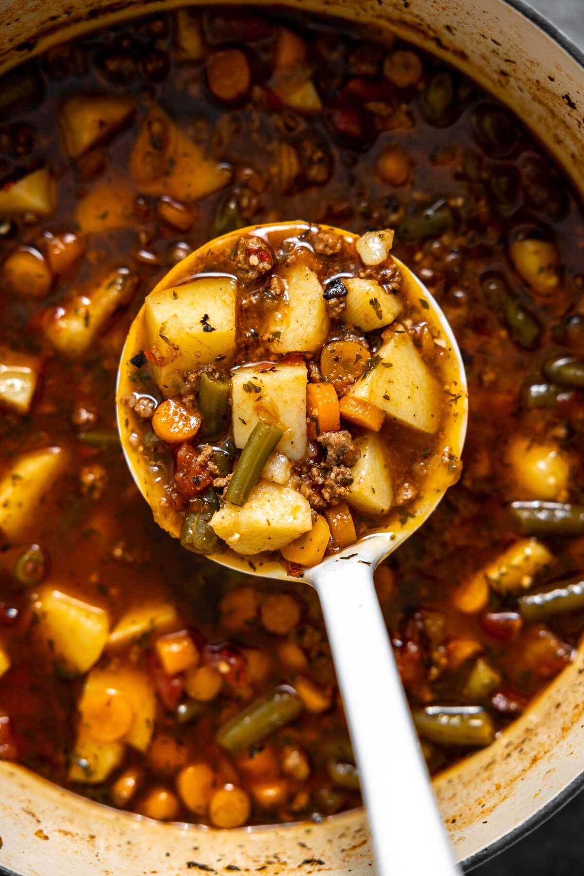 A ladle bringing a ladle-full of hamburger soup out of the pot. 