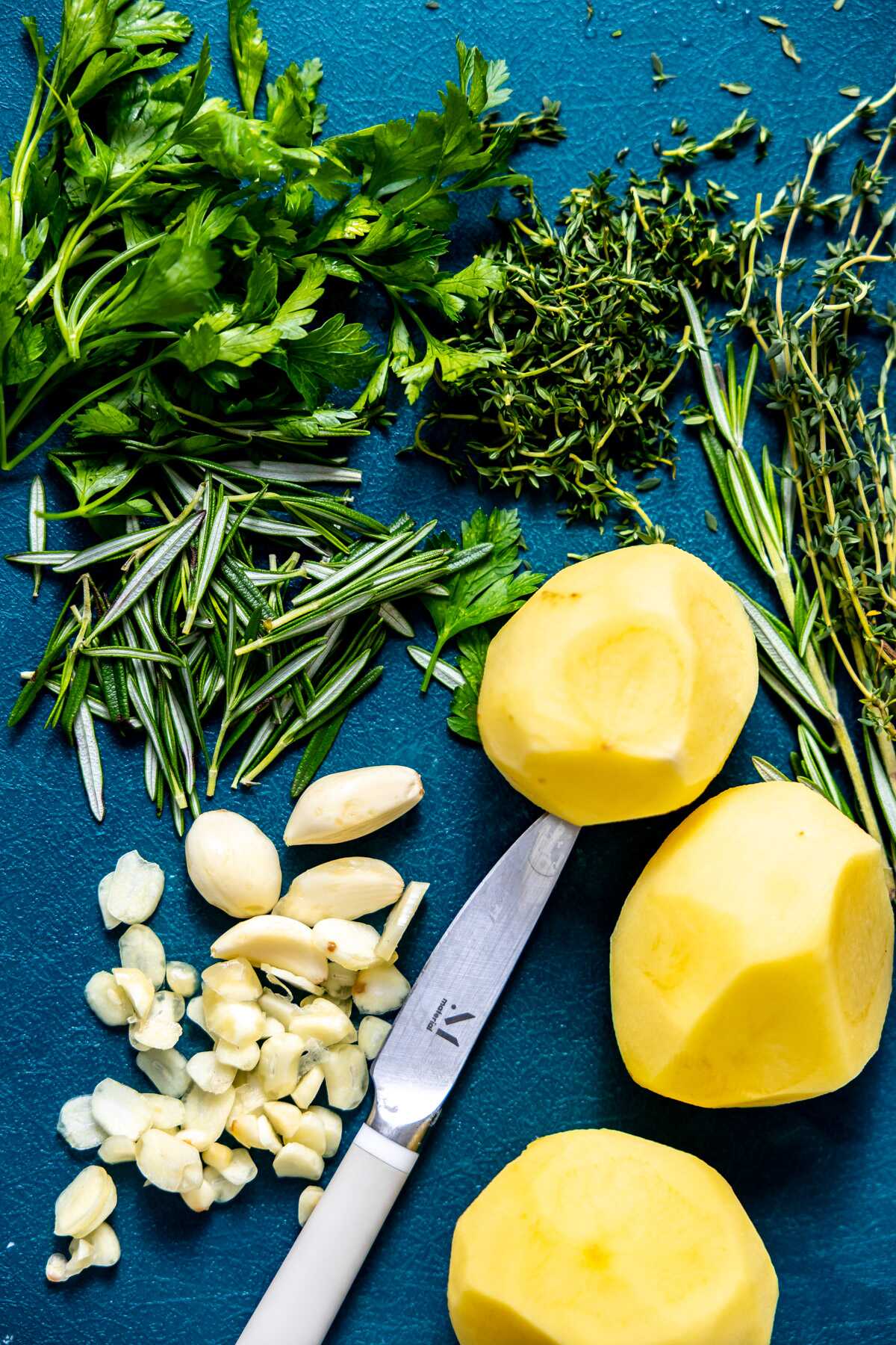 Peeled potatoes, chopped garlic and herbs on a cutting board. 