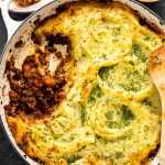A shepherd's pie in a large skillet with a serving taken out of it exposing the ground beef mixture underneath the potatoes.