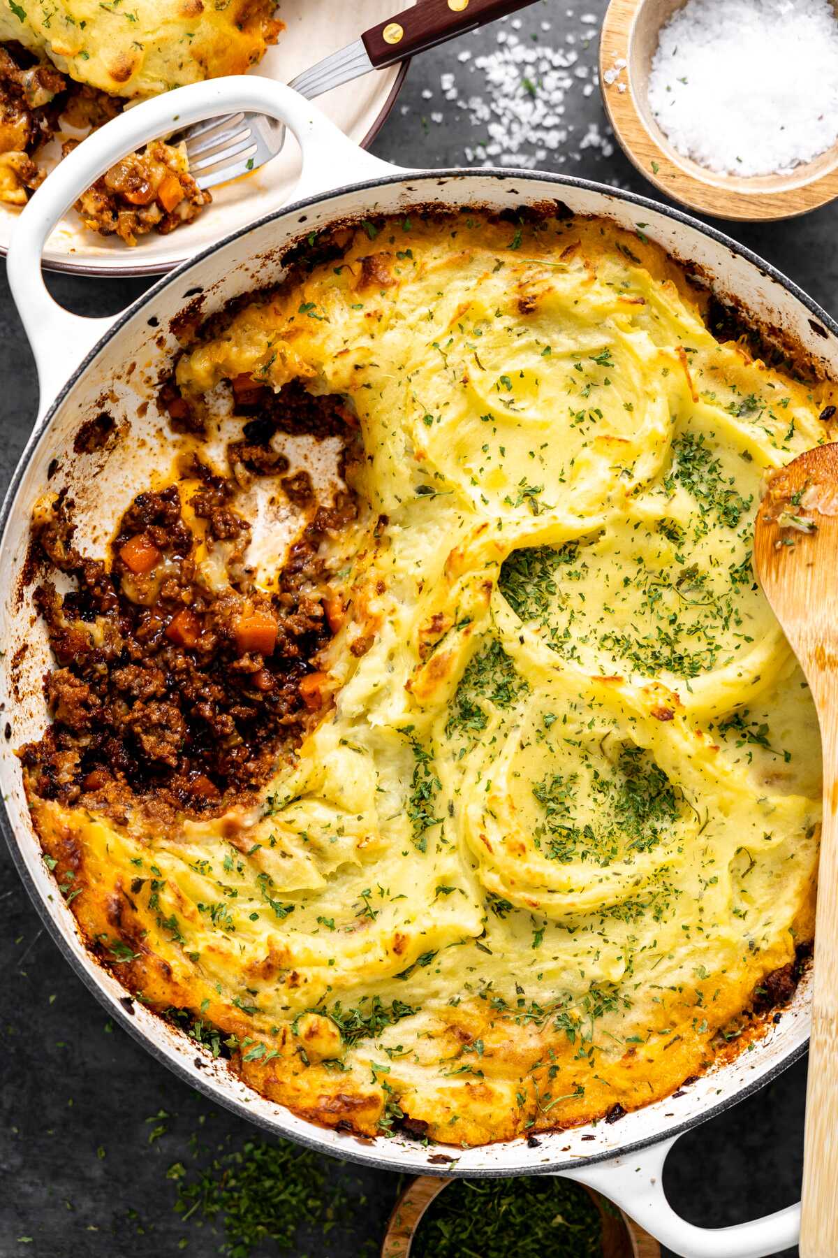 A shepherd's pie in a large skillet with a serving taken out of it exposing the ground beef mixture underneath the potatoes. 