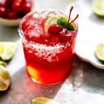 A cherry limeade margarita topped with lime wedges and cherries.