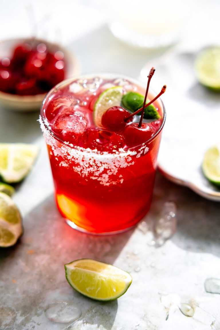 A cherry limeade margarita topped with lime wedges and cherries.