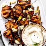 Dill pickle grilled chicken thighs on a platter with chopped dill and pickles.
