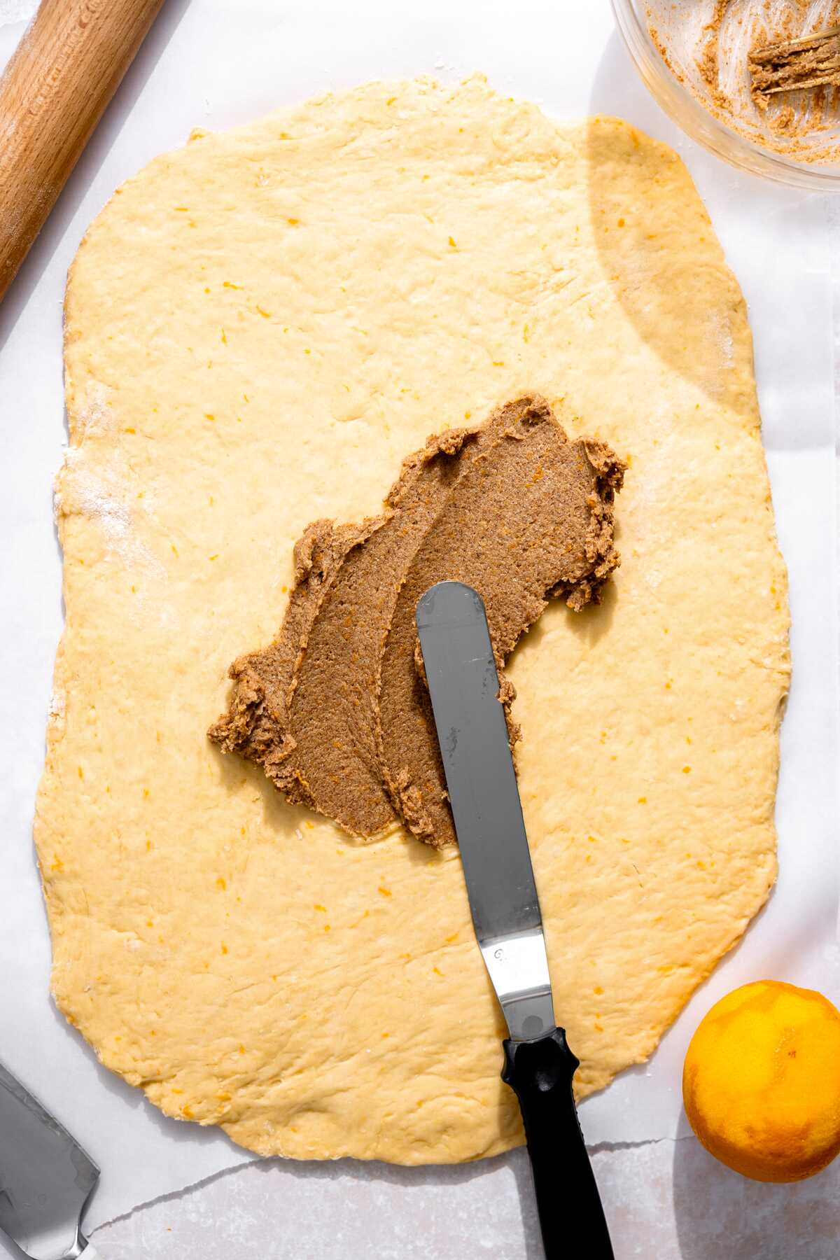 Orange roll dough rolled out with the buttery sugar filling being spread over the top.