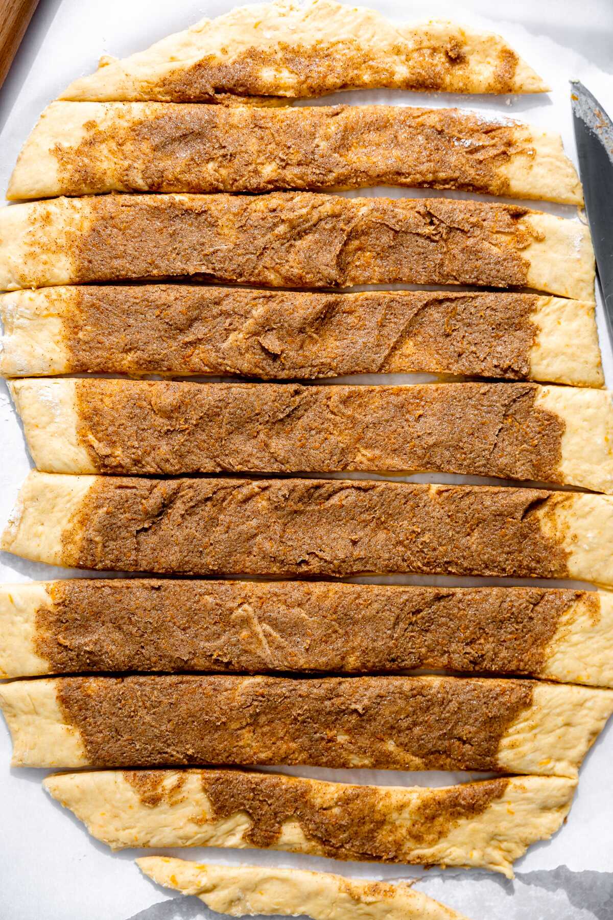 Orange roll dough cut into strips ready to be rolled up.
