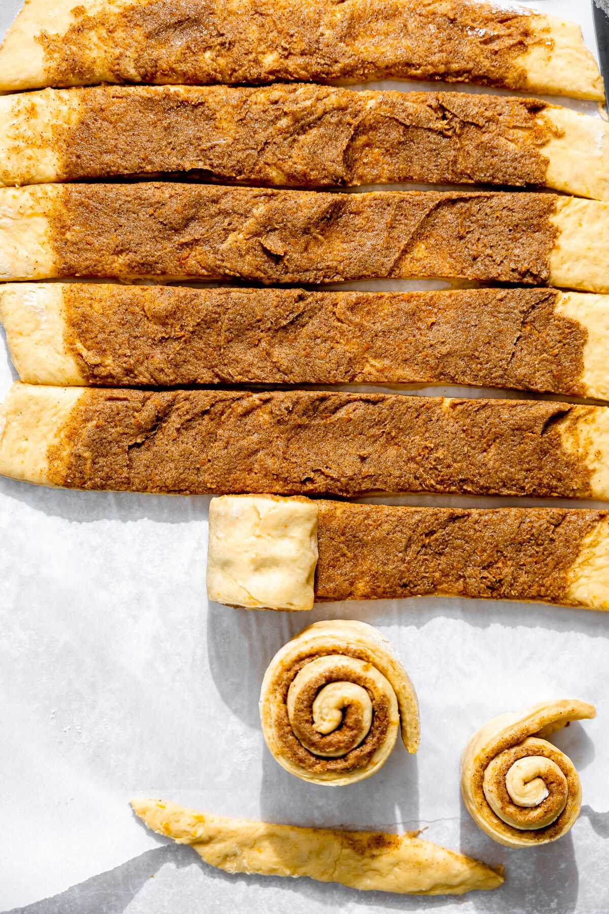 Orange roll dough being rolled up into cinnamon rolls.