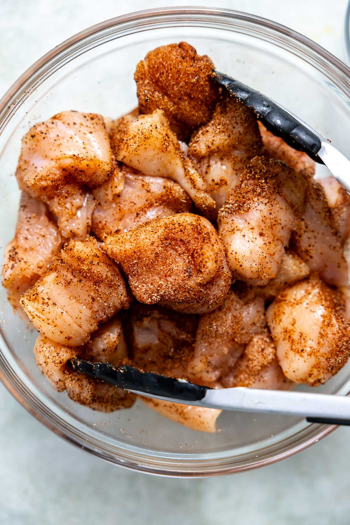 Cubed chicken in a bowl with seasonings. 