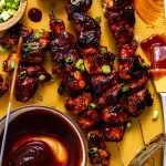BBQ chicken skewers on a serving board with bbq sauce and green onions.