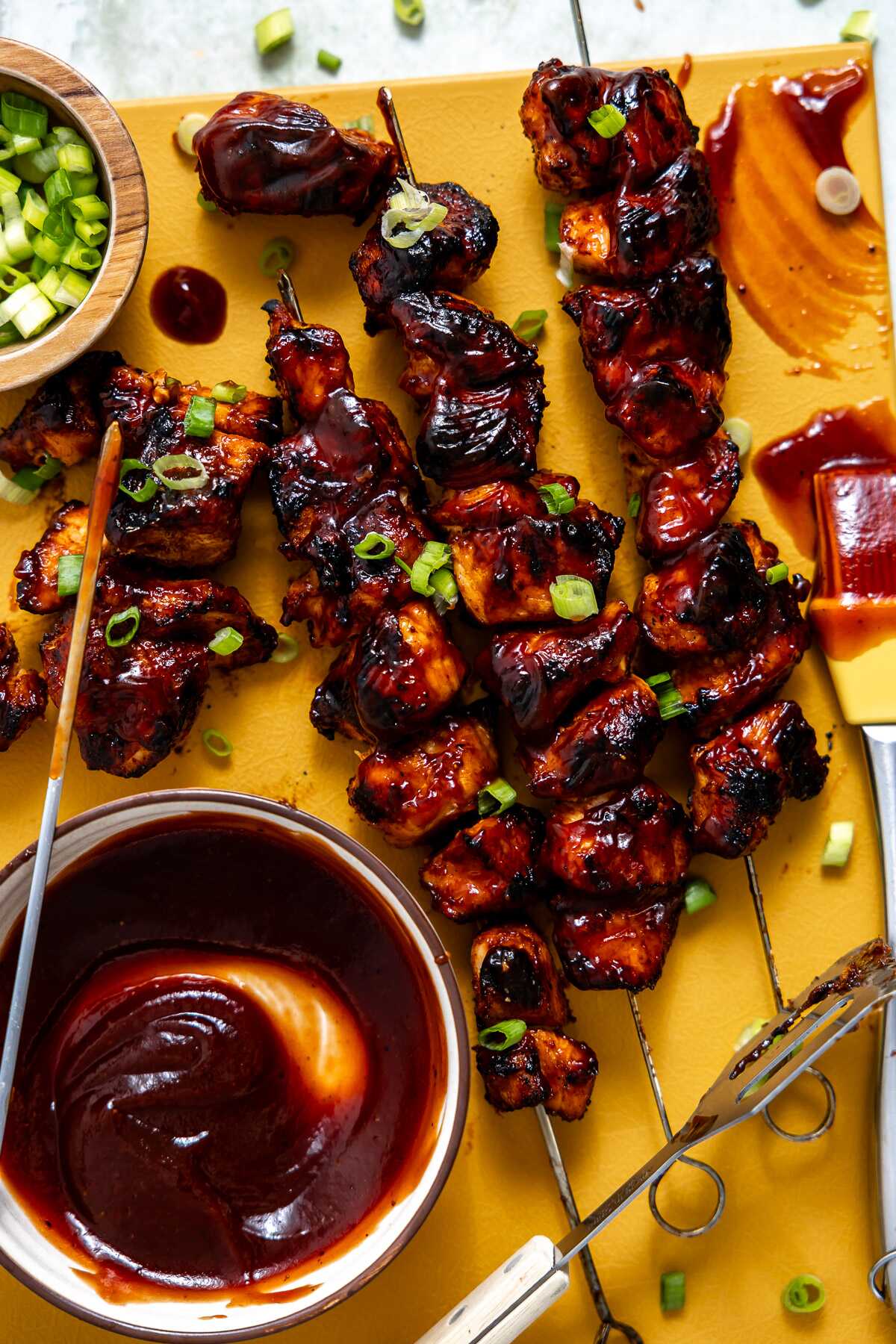 BBQ chicken skewers on a serving board with bbq sauce and green onions.
