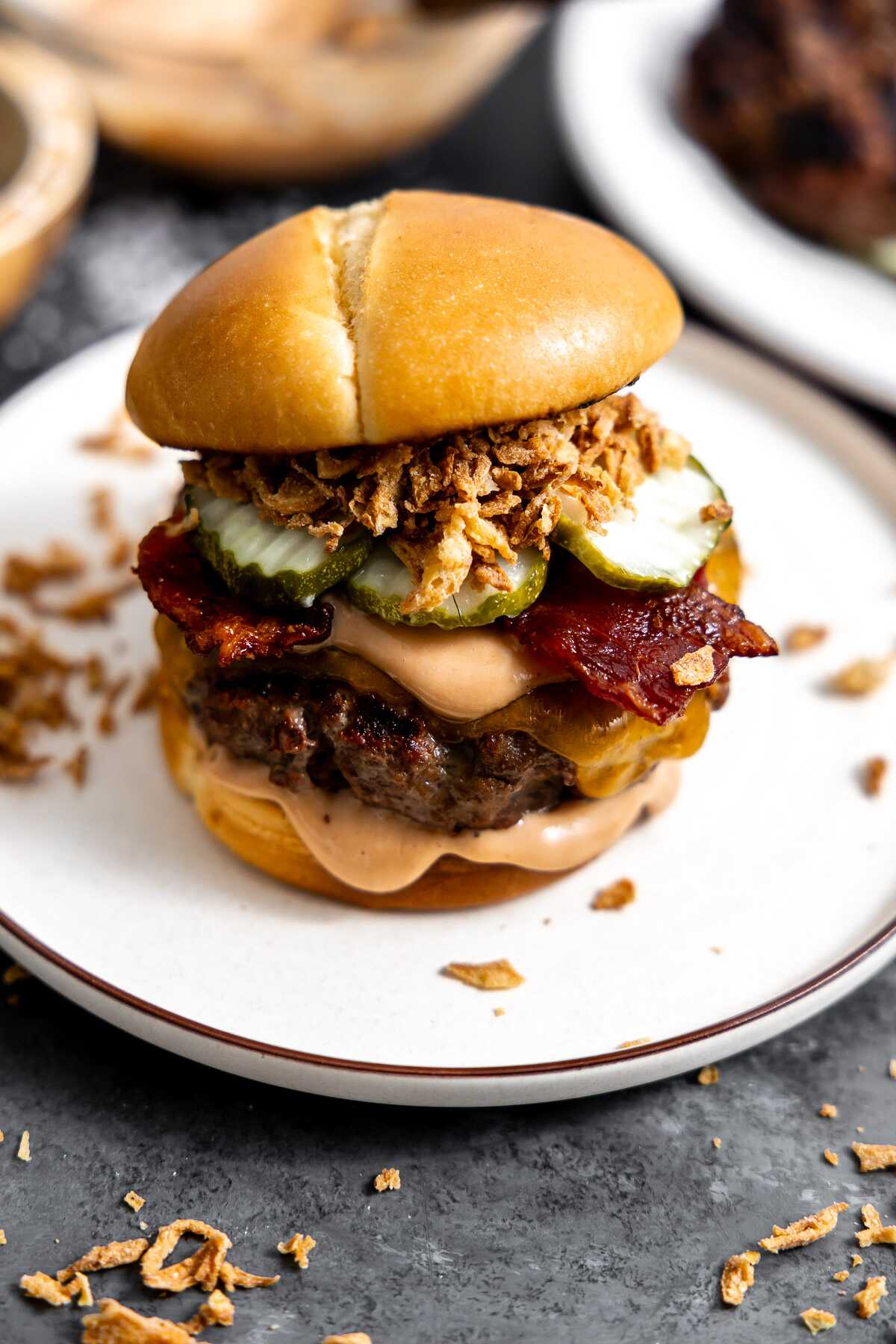 A cowboy burger loaded with sauce, bacon, pickles and french fried onions on a bun.