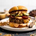 A cowboy burger loaded with sauce, bacon, pickles and french fried onions on a bun.