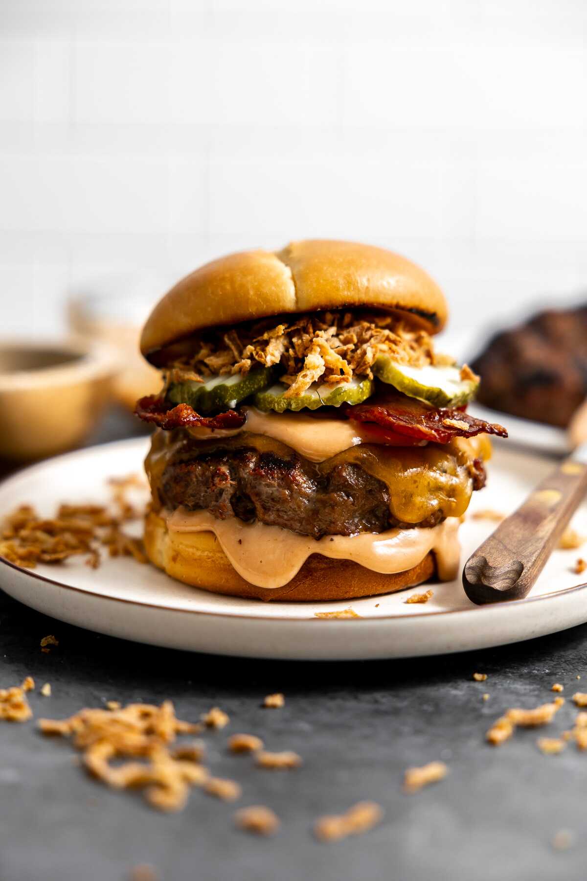 A cowboy burger loaded with sauce, bacon, pickles and french fried onions on a bun.
