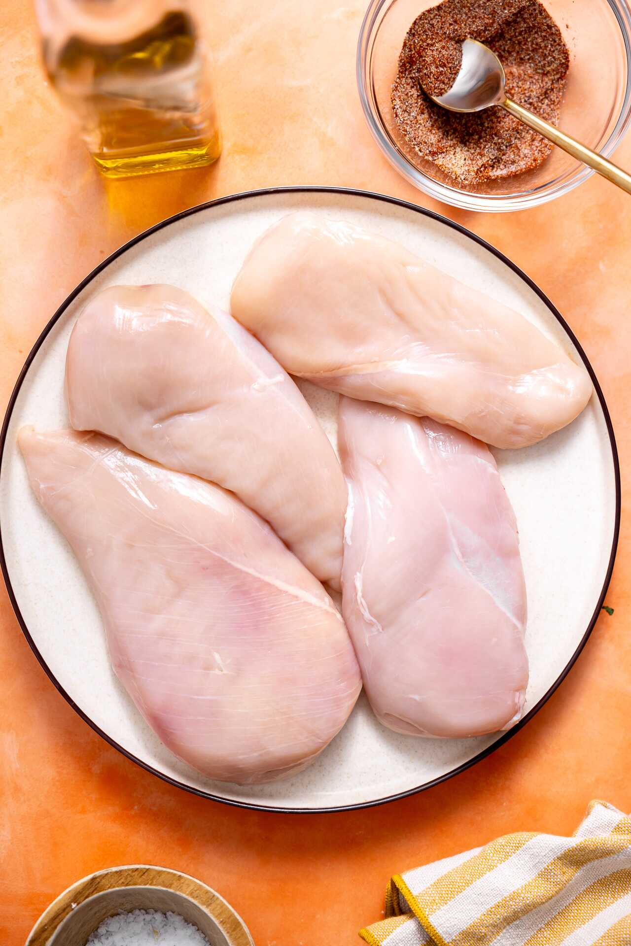 Chicken breasts on a plate with seasoning ingredients around. 
