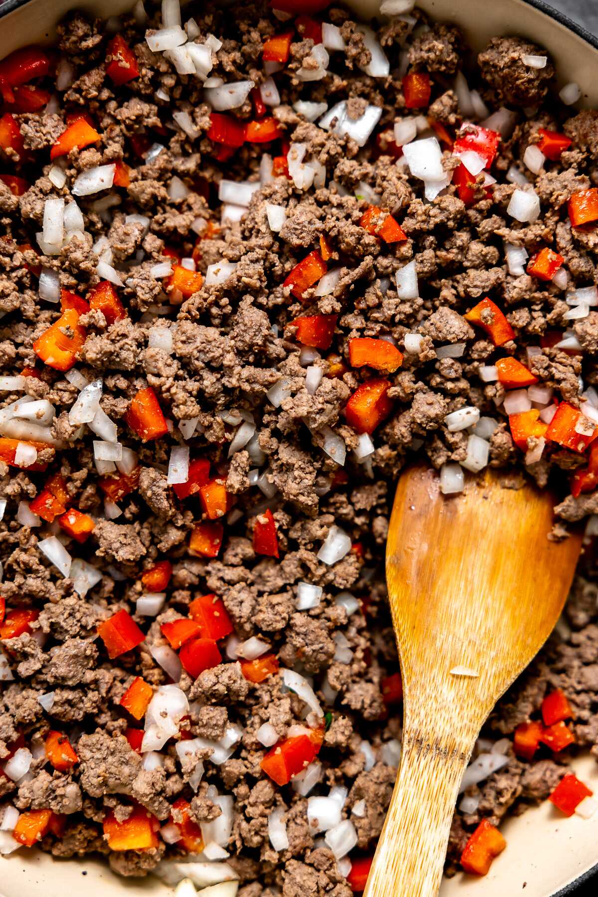 Ground beef sautéd in a skillet with onion and red bell pepper.